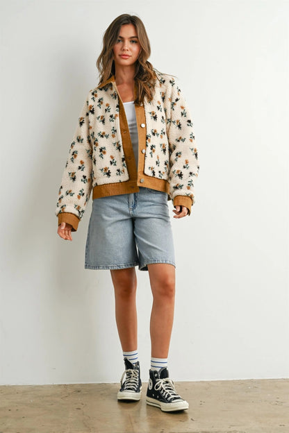 A women's cream floral printed plush sherpa fleece jacket featuring camel brown twill contrast trim, front button closures, and side pockets.