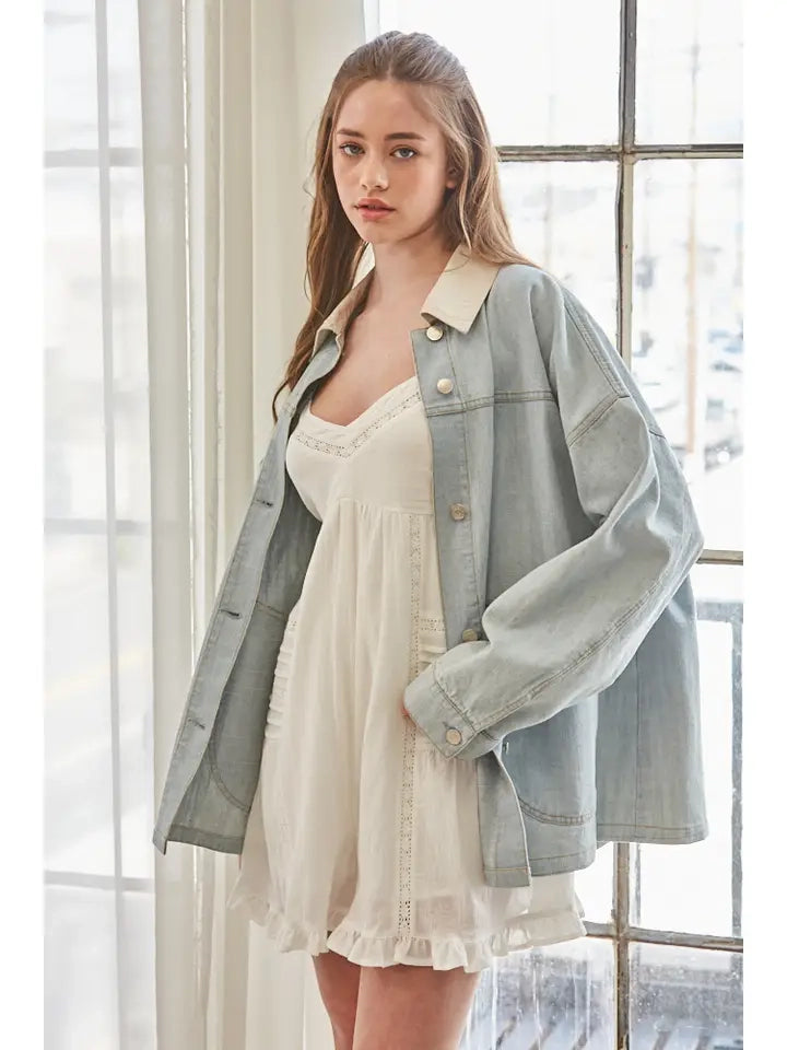 A women's relaxed oversized light wash denim utility jacket featuring a cream-colored pointed contrast collar, a button-front closure, and large front patch pockets with flaps.