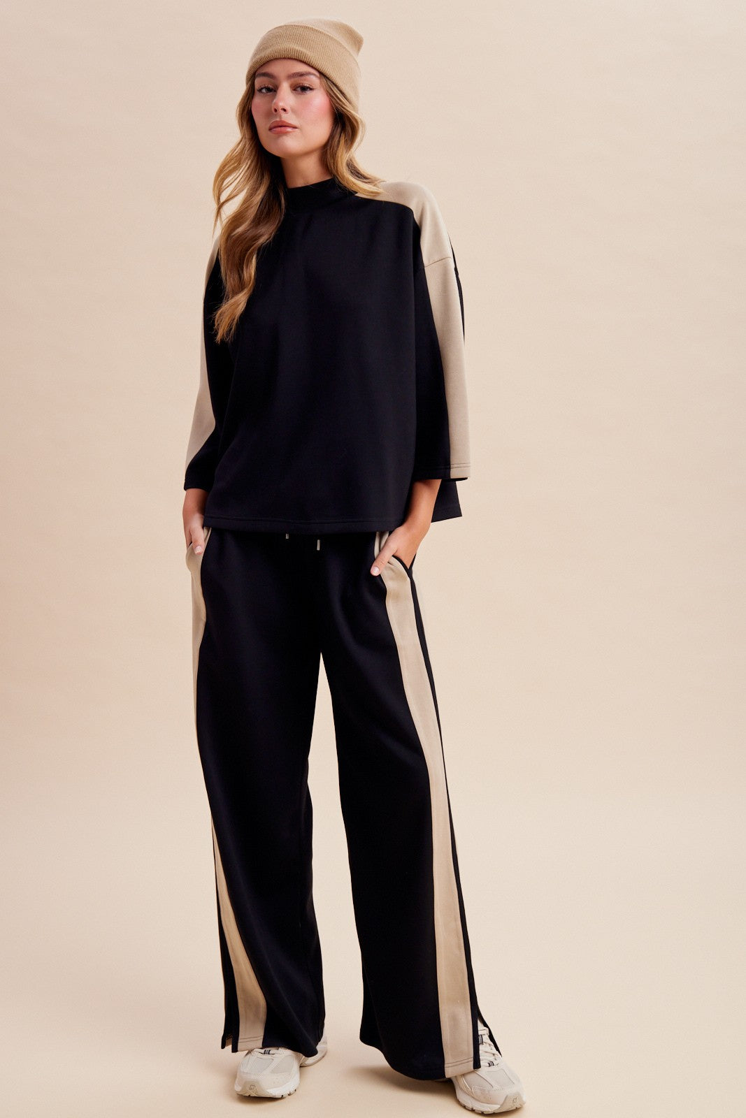 Women's two-piece black lounge set featuring a half-sleeve mock-neck top, neutral side-stripe detailing, and matching wide-leg pants with ankle hem slits.