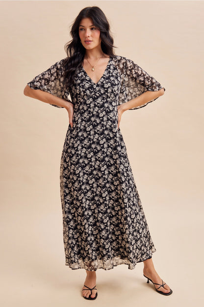 A women's v-neck maxi dress in a black and cream floral print featuring short flutter sleeves and an empire waist silhouette.