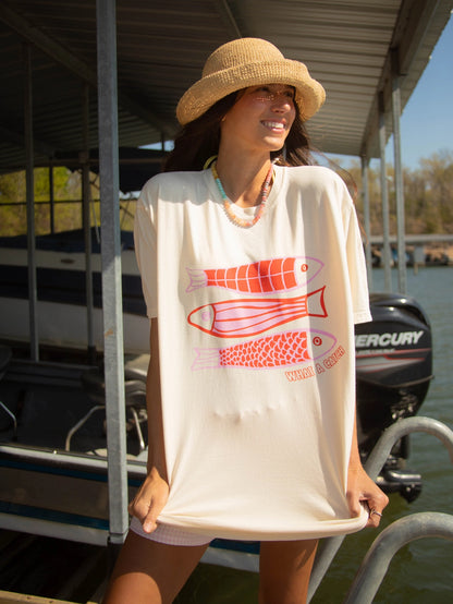 A women's oversized relaxed-fit cream graphic t-shirt featuring three stacked fish illustrations in shades of coral, pink, and red with the phrase "What A Catch" printed in the bottom right corner.