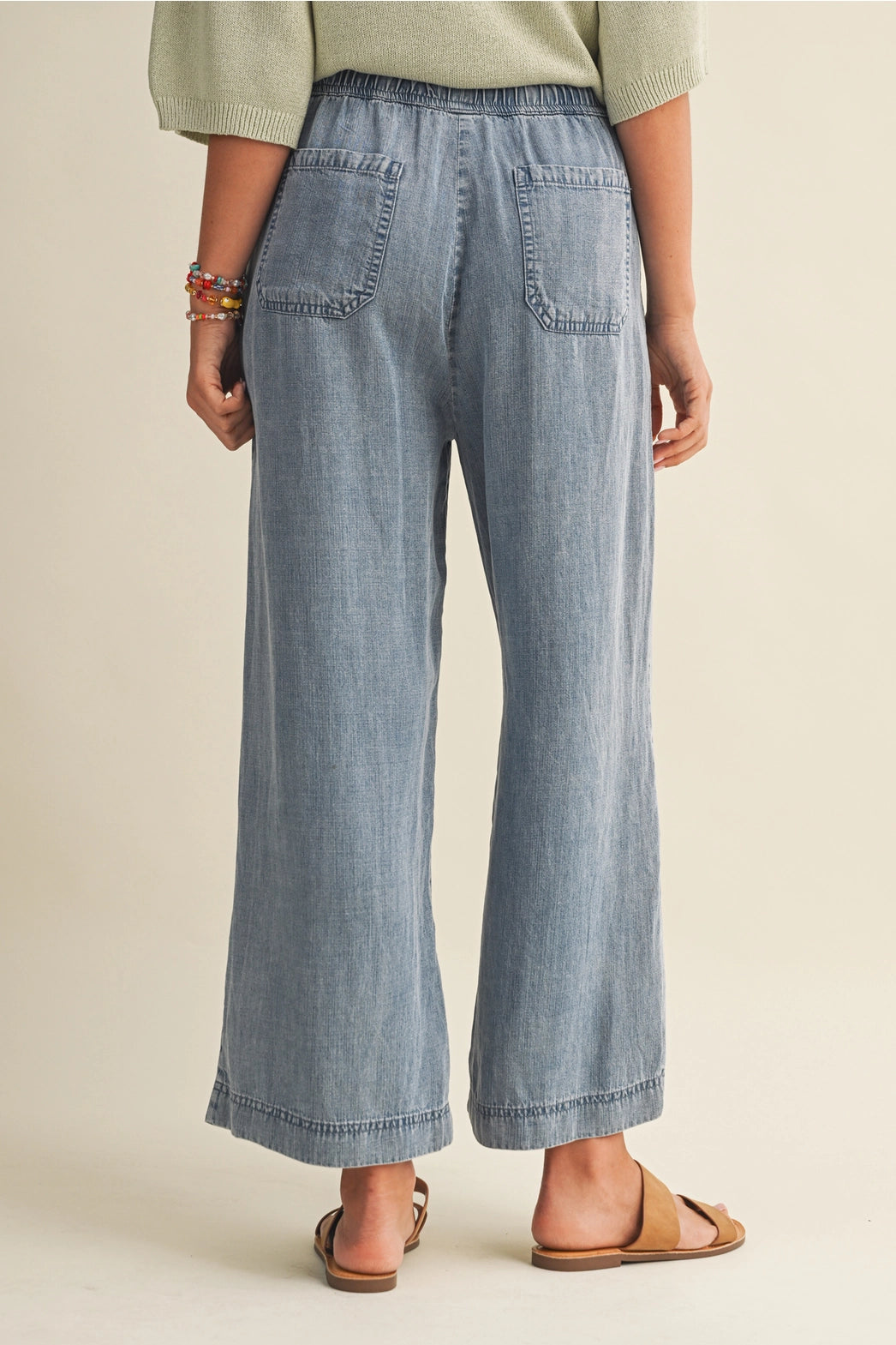 A pair of women's high-waisted wide-leg denim chambray pants featuring a gathered elastic drawstring waistband and functional front patch pockets.