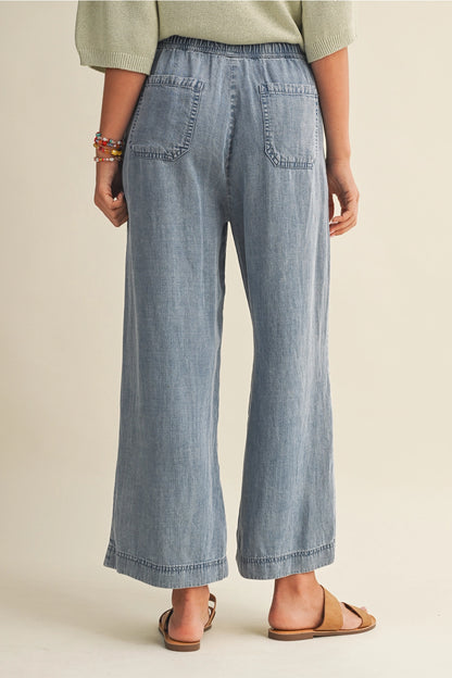 A pair of women's high-waisted wide-leg denim chambray pants featuring a gathered elastic drawstring waistband and functional front patch pockets.