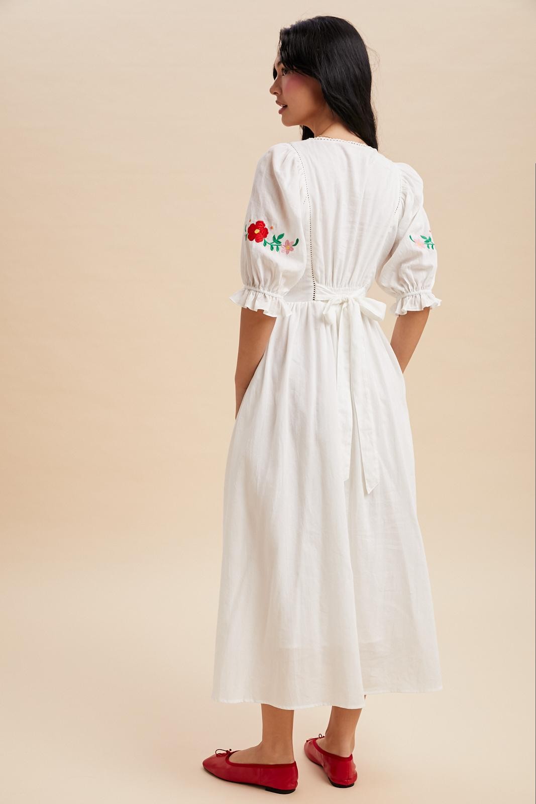Off white maxi dress with a v-neck and embroidered bodice.  The sleeves are cuffed with a ruffle detail and hit just above the elbow with minimal embroidered detail. Waist tie in the back. 