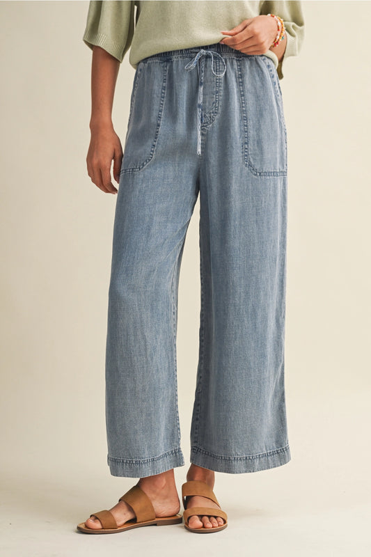 A pair of women's high-waisted wide-leg denim chambray pants featuring a gathered elastic drawstring waistband and functional front patch pockets.