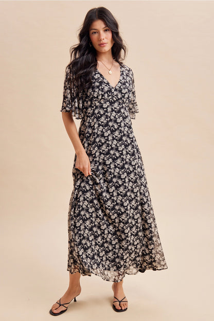 A women's v-neck maxi dress in a black and cream floral print featuring short flutter sleeves and an empire waist silhouette.