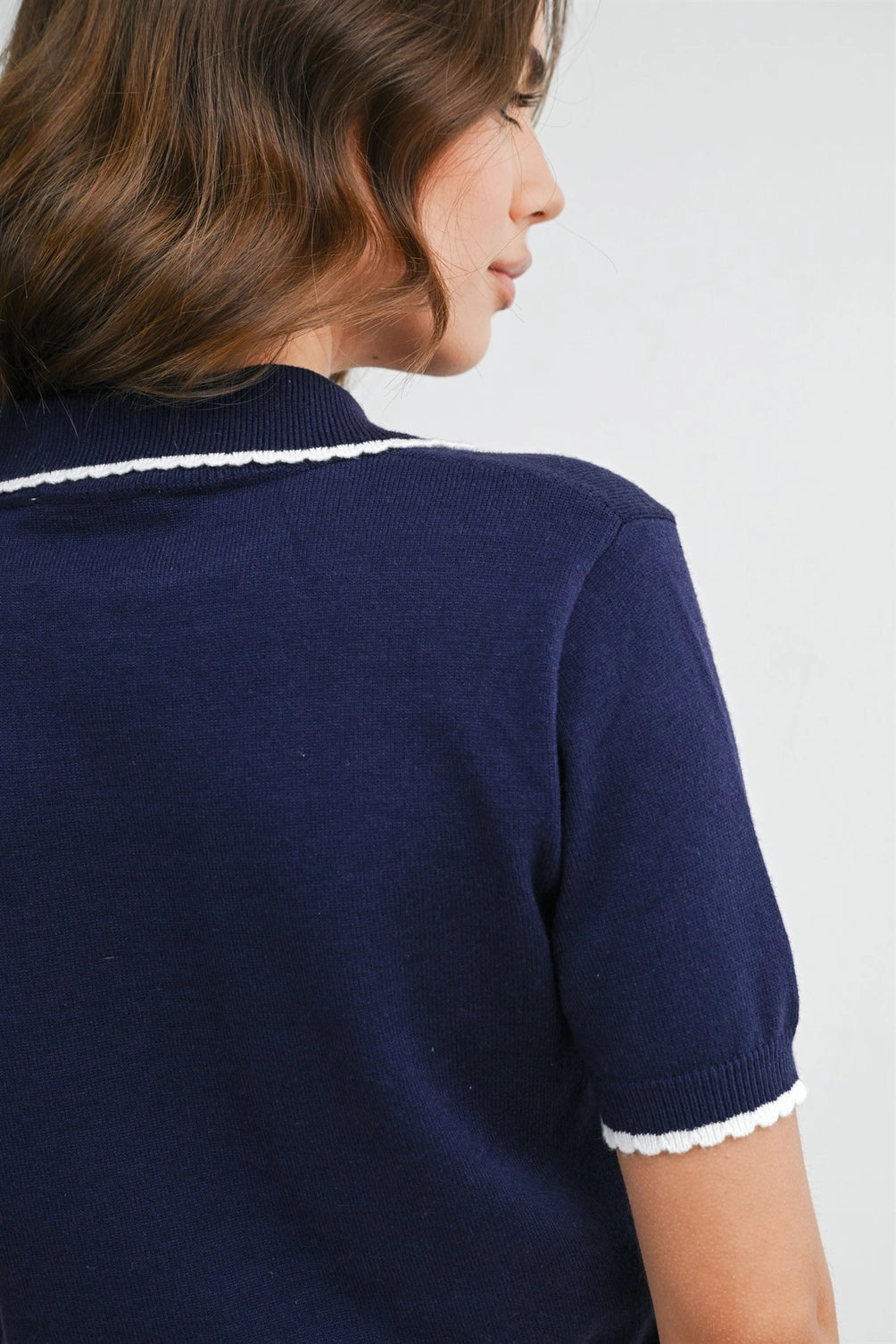 A women's navy blue short-sleeve fine-knit polo top featuring white scalloped contrast trim on the collar, button placket, and sleeve cuffs.