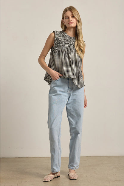 A women's sleeveless black and white gingham check blouse featuring a smocked high mock neckline, ruffle shoulder details, and a relaxed baby-doll silhouette.