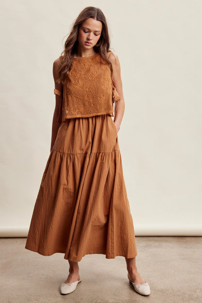 A women's brown sleeveless tiered maxi dress featuring a tonal embroidered floral lace vest overlay with adjustable side tie details.