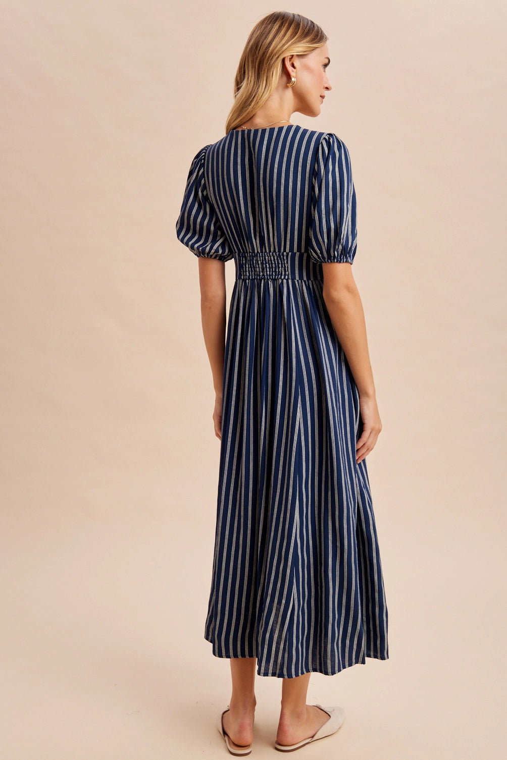 A women's navy blue and cream vertically striped short puff sleeve maxi dress featuring a V-neckline, full front button placket, and high gathered waistline.