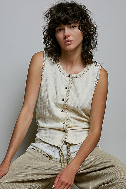 A women's sleeveless cream textured waffle-knit top featuring a button-front closure and delicate eyelet lace trimming along the round neckline and armholes.