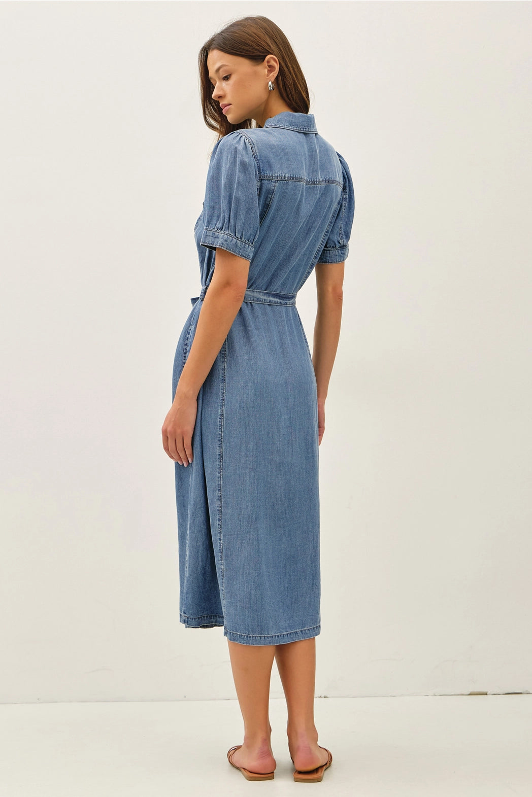 A women's short puff-sleeve denim shirt dress in a light wash featuring a pointed collar, a full button-down front, a matching waist tie belt, and convenient side pockets.