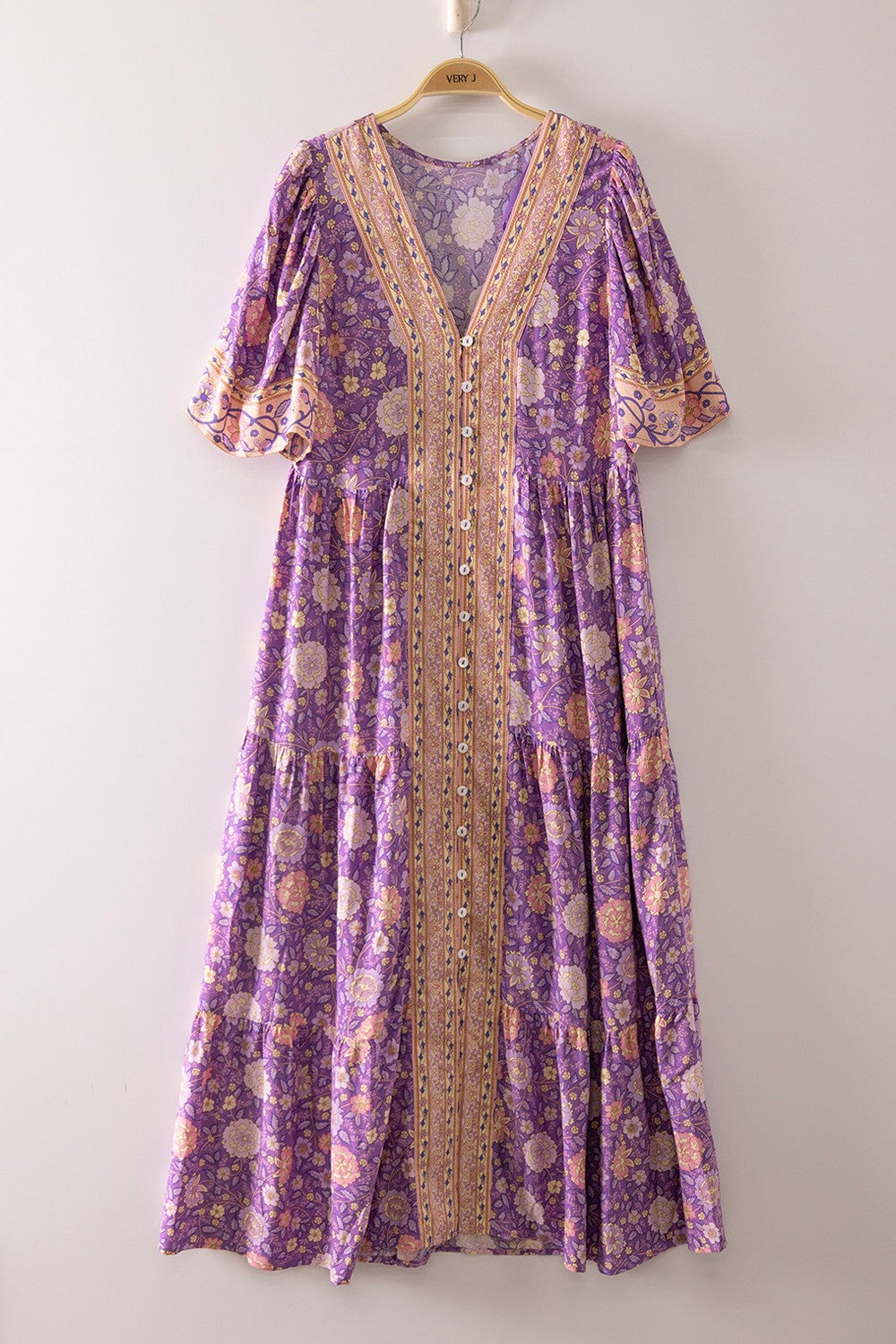 A short-sleeve tiered floral maxi dress in a lavender, coral, and gold mix featuring a deep V-neckline, button-down front closure, and decorative border print detailing.