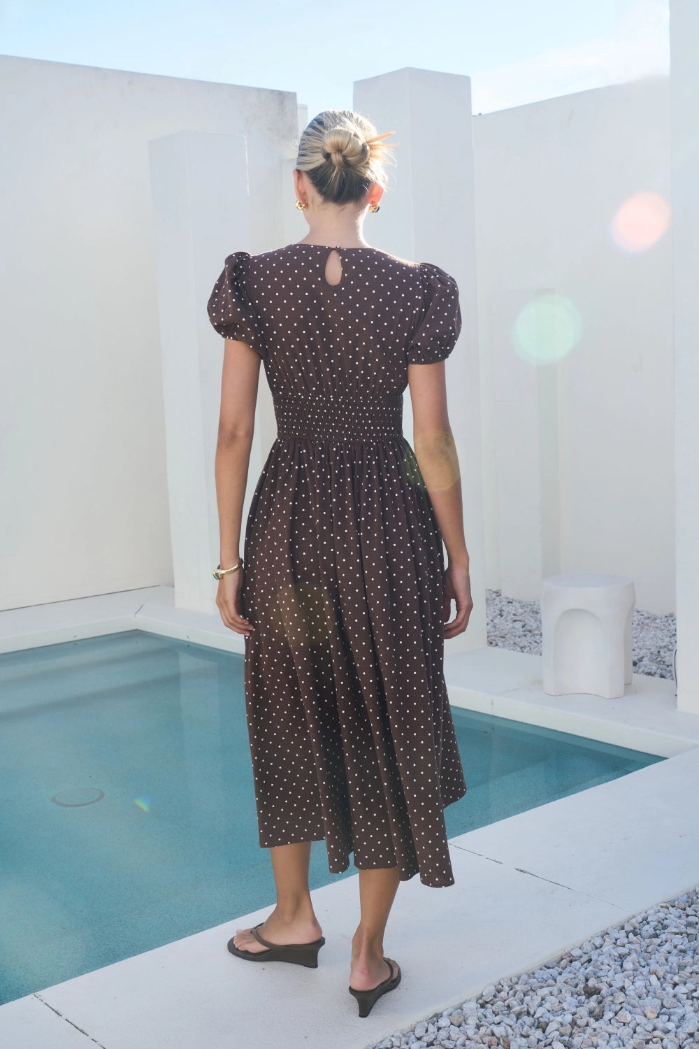 A short-sleeve brown and white polka dot midi dress featuring a V-neckline with a keyhole front tie detail, structured puff sleeves, and functional side pockets.