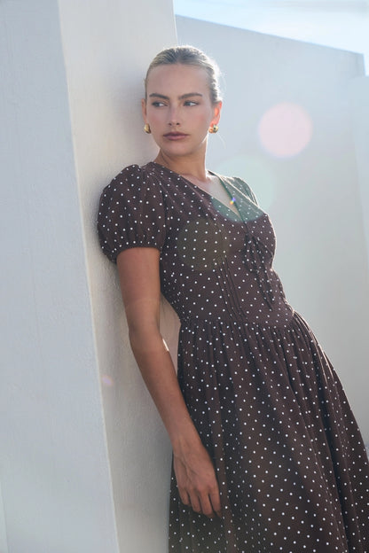 A short-sleeve brown and white polka dot midi dress featuring a V-neckline with a keyhole front tie detail, structured puff sleeves, and functional side pockets.
