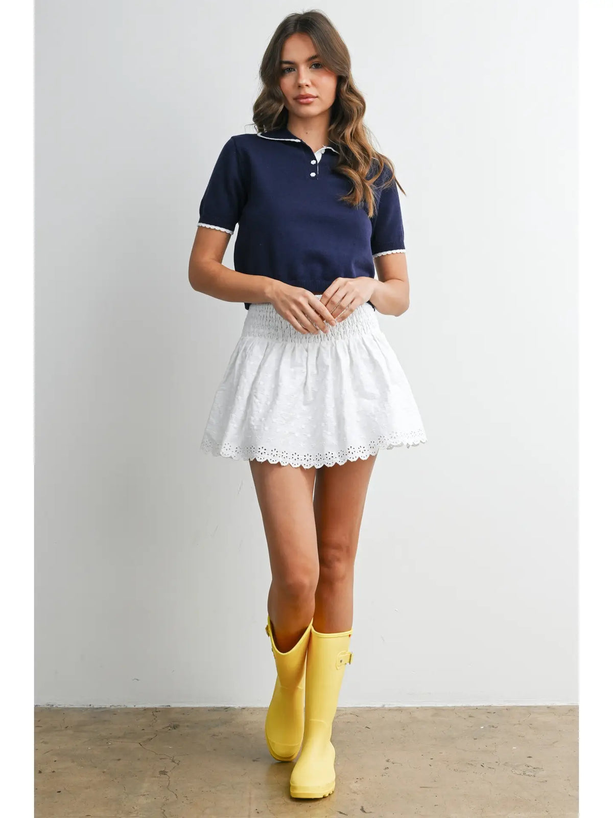 A women's navy blue short-sleeve fine-knit polo top featuring white scalloped contrast trim on the collar, button placket, and sleeve cuffs.