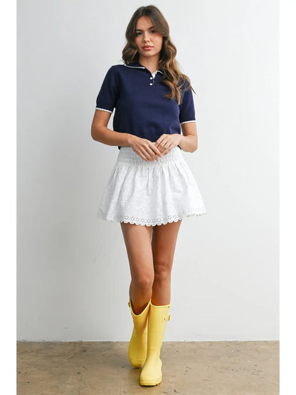 A women's navy blue short-sleeve fine-knit polo top featuring white scalloped contrast trim on the collar, button placket, and sleeve cuffs.