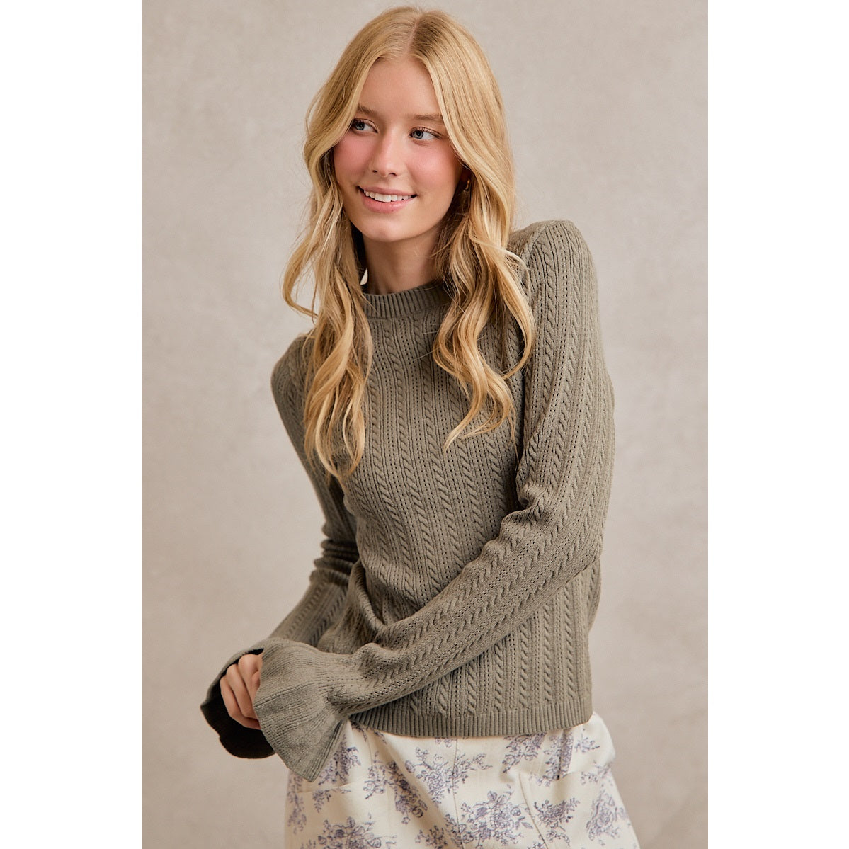A women's olive green long-sleeve cable-knit sweater featuring a mock neckline, ribbed hem, and ruffled flare knit cuffs.