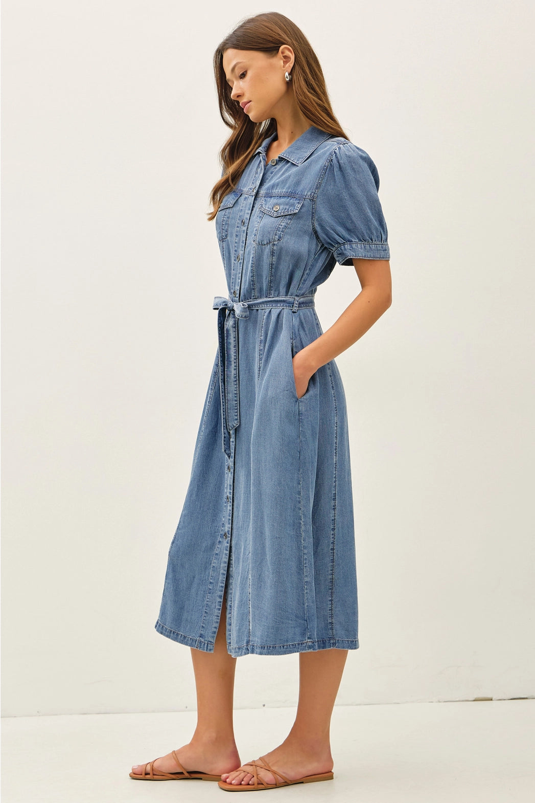A women's short puff-sleeve denim shirt dress in a light wash featuring a pointed collar, a full button-down front, a matching waist tie belt, and convenient side pockets.