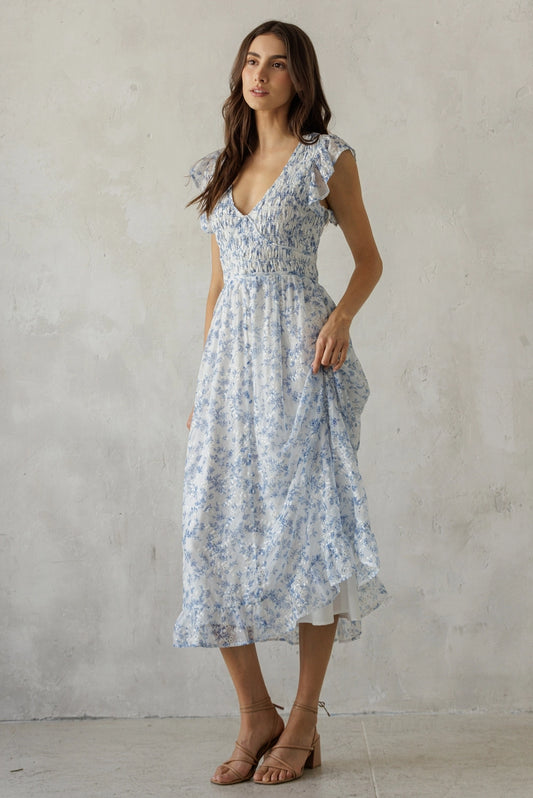 A dainty blue and white floral midi dress featuring a stretchy smocked bodice, delicate flutter ruffle sleeves, and a breezy tiered skirt.