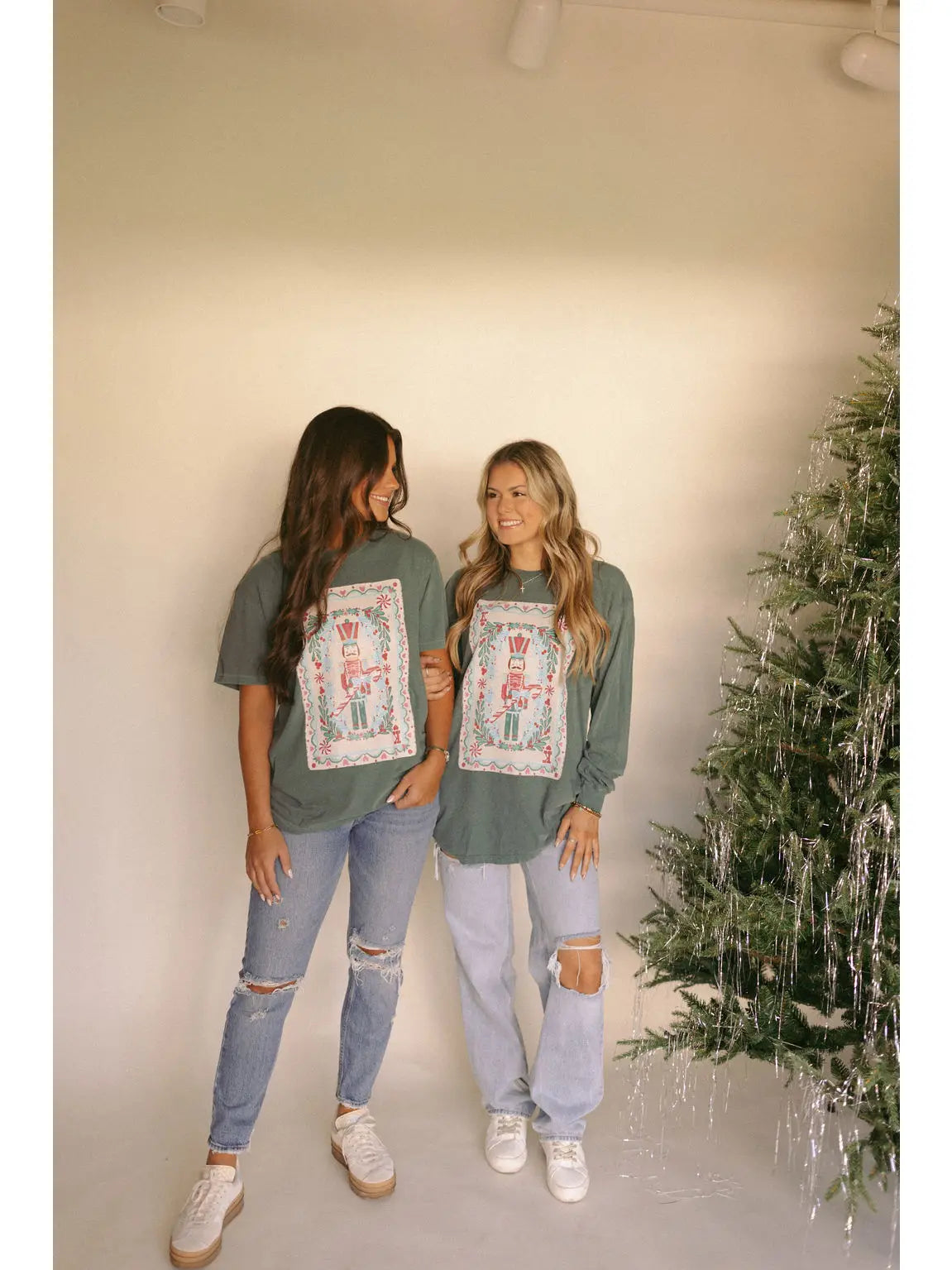 A women's gray sage green long-sleeve cotton graphic tee featuring a vintage-inspired holiday nutcracker playing card design with botanical greenery and pink accents.