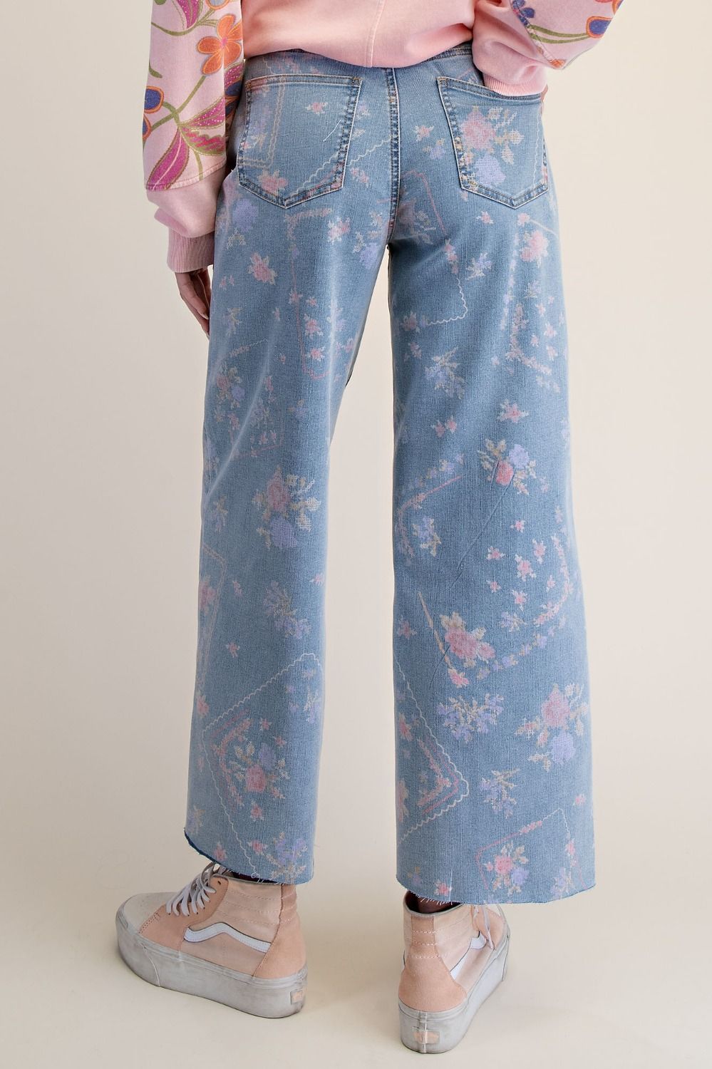 A pair of women's high-waisted wide-leg stretch denim jeans in a light wash featuring an all-over purple and pink floral print and frayed raw hems.