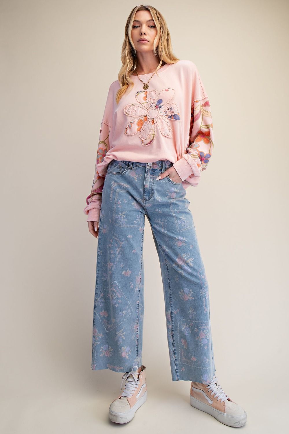 A pair of women's high-waisted wide-leg stretch denim jeans in a light wash featuring an all-over purple and pink floral print and frayed raw hems.