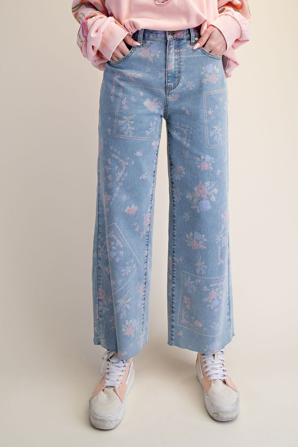 A pair of women's high-waisted wide-leg stretch denim jeans in a light wash featuring an all-over purple and pink floral print and frayed raw hems.