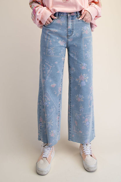 A pair of women's high-waisted wide-leg stretch denim jeans in a light wash featuring an all-over purple and pink floral print and frayed raw hems.