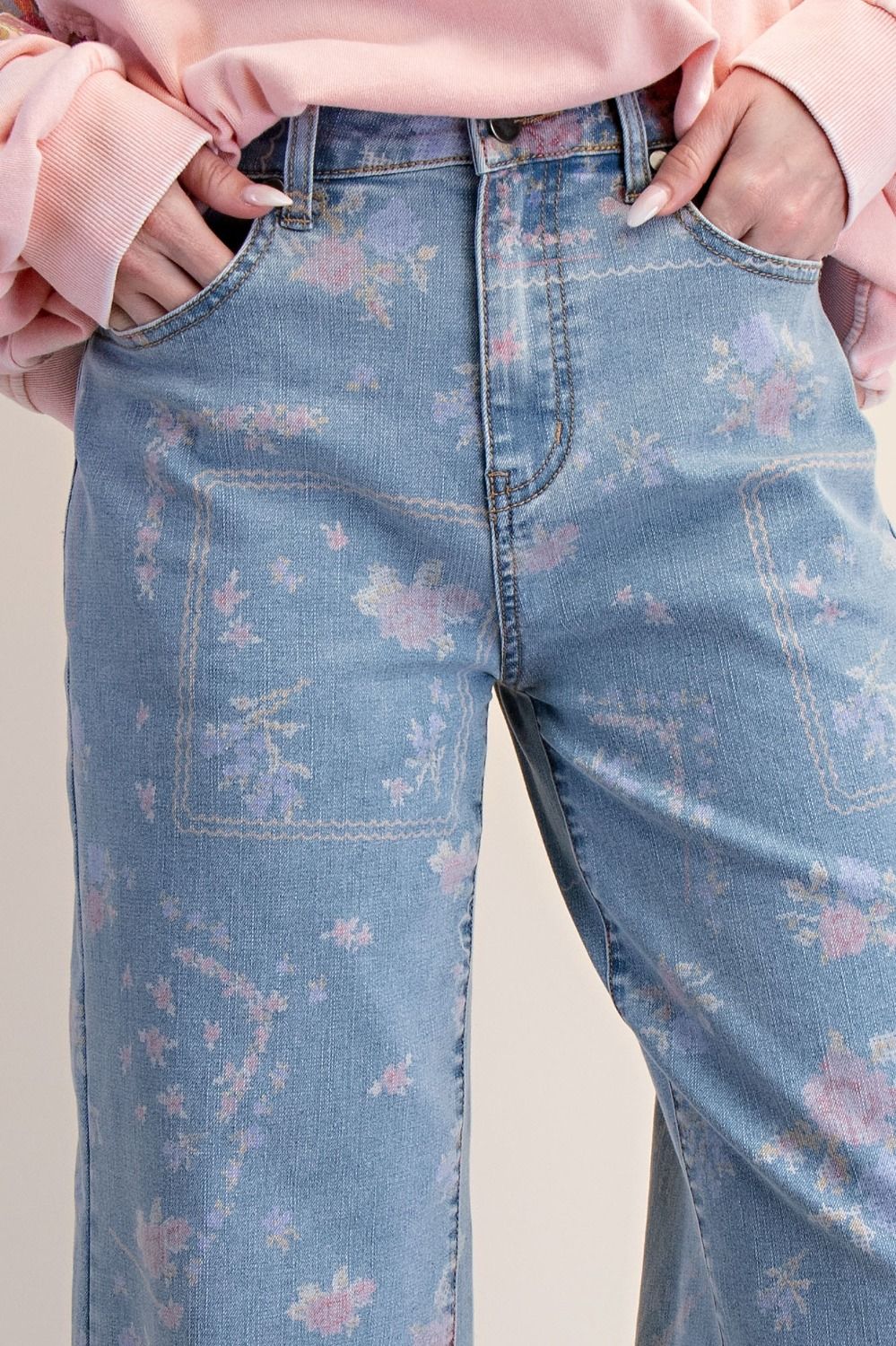 A pair of women's high-waisted wide-leg stretch denim jeans in a light wash featuring an all-over purple and pink floral print and frayed raw hems.