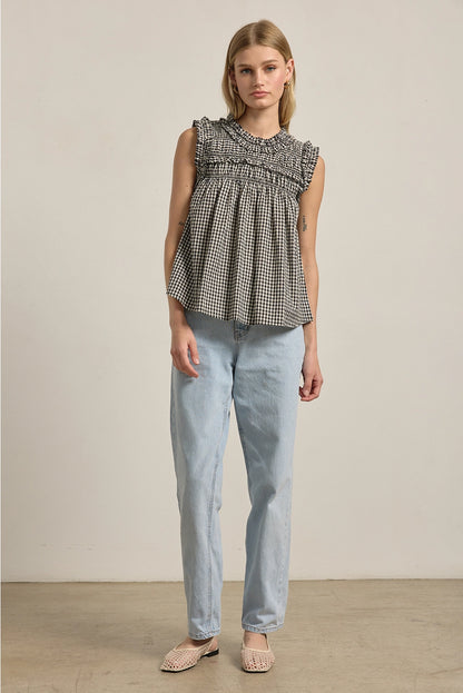 A women's sleeveless black and white gingham check blouse featuring a smocked high mock neckline, ruffle shoulder details, and a relaxed baby-doll silhouette.