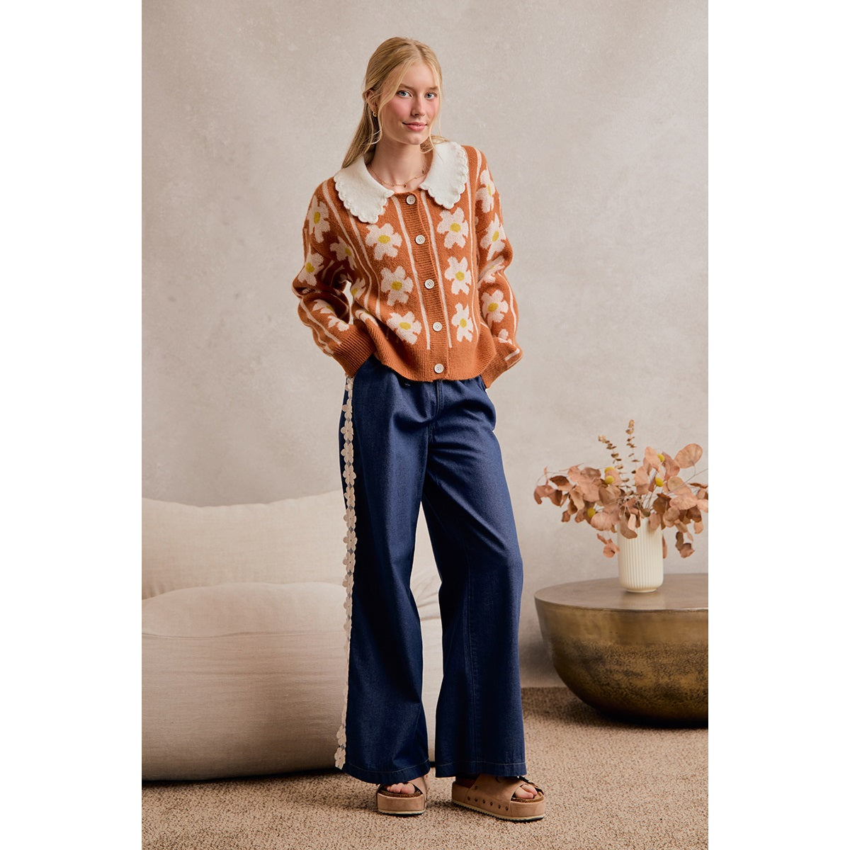 A women's medium wash wide-leg denim pants featuring a gathered elastic drawstring waistband and white crochet daisy floral lace side seam trim.
