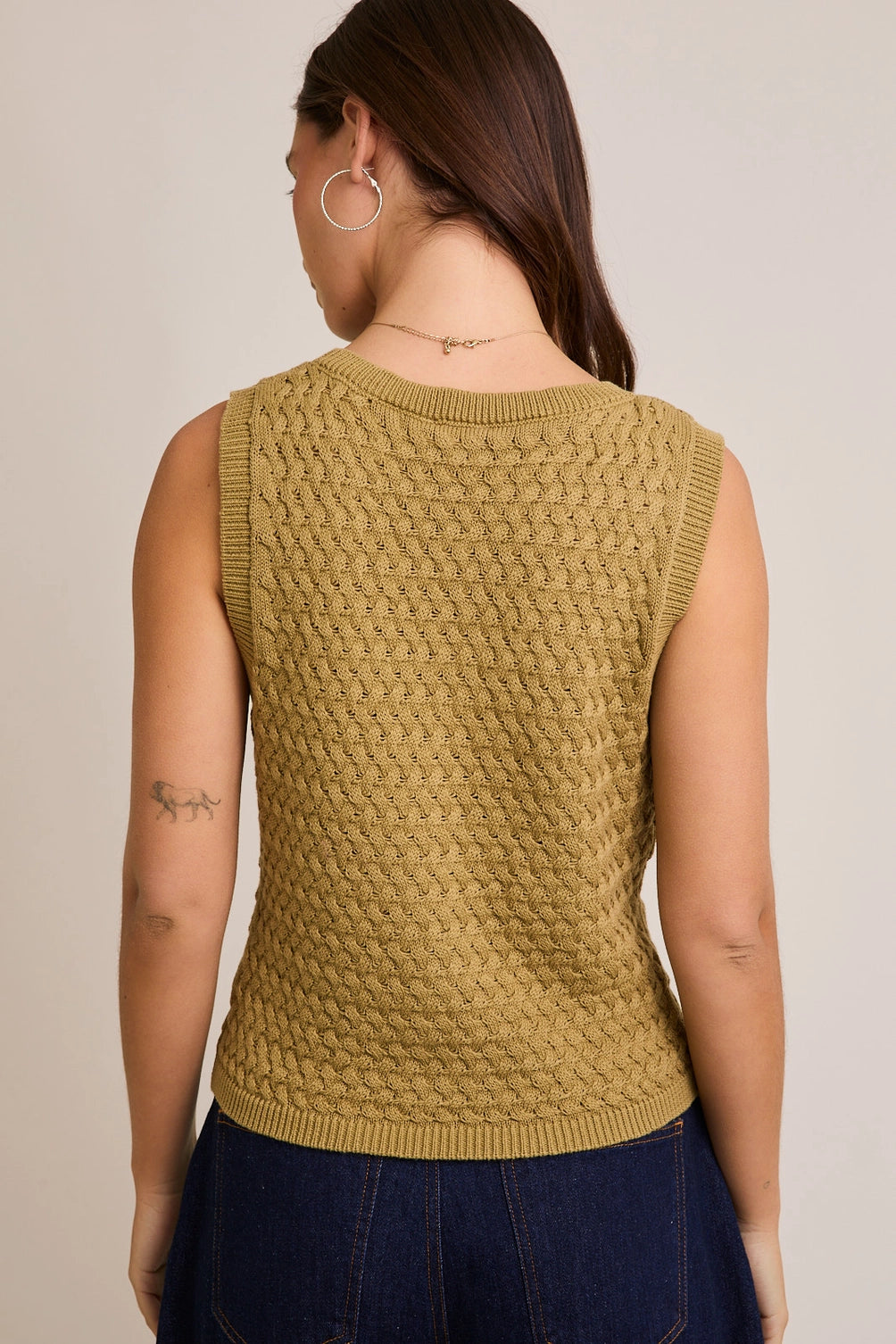 A women's sleeveless olive green button-front vest knit top featuring an intricate textured basketweave pattern, a modest V-neckline, and ribbed trim along the split hem.