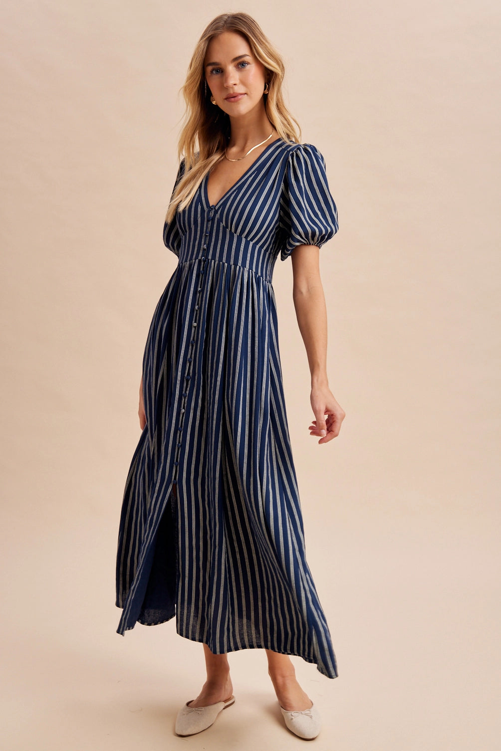 A women's navy blue and cream vertically striped short puff sleeve maxi dress featuring a V-neckline, full front button placket, and high gathered waistline.