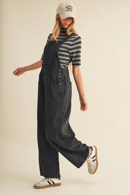 A pair of women's high-waisted wide-leg twill overalls in a vintage washed black denim finish featuring classic adjustable shoulder straps, a front chest pocket, and side pockets.