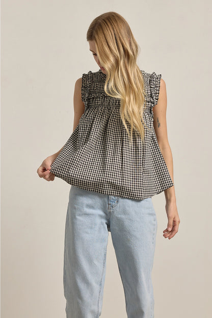 A women's sleeveless black and white gingham check blouse featuring a smocked high mock neckline, ruffle shoulder details, and a relaxed baby-doll silhouette.