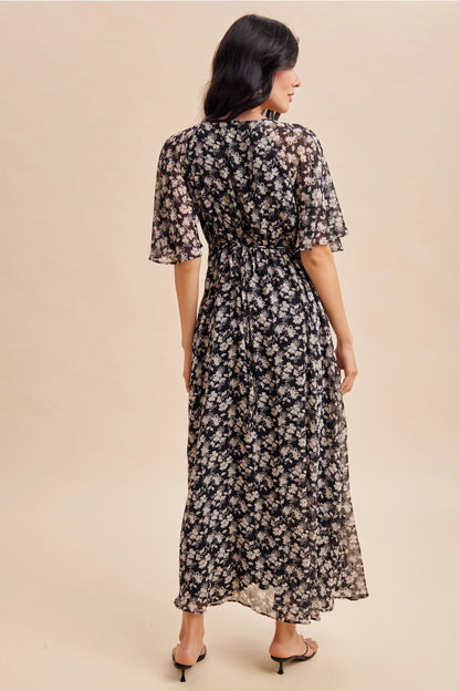 A women's v-neck maxi dress in a black and cream floral print featuring short flutter sleeves and an empire waist silhouette.