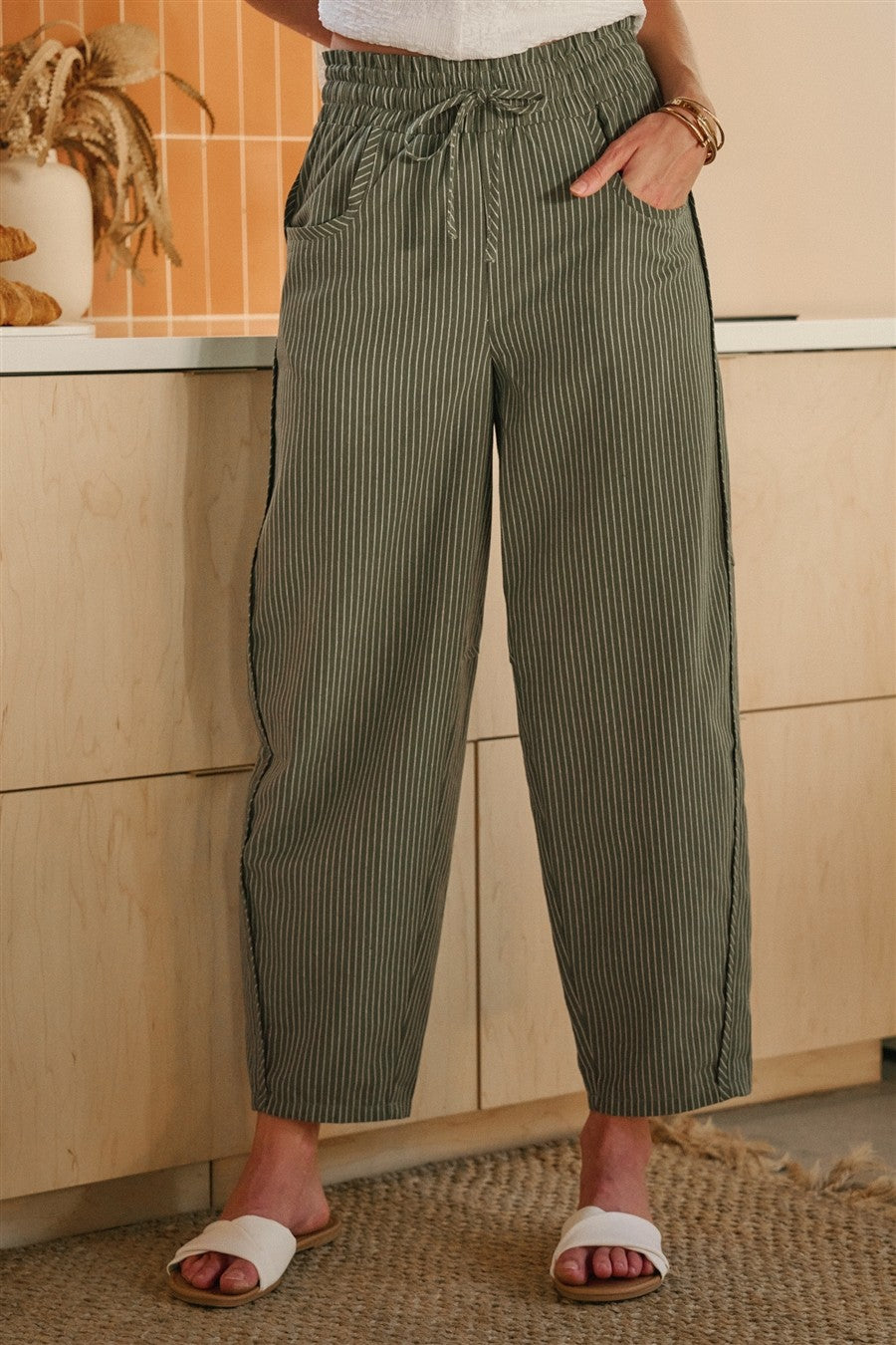 Olive and oatmeal vertical striped linen-blend pants featuring a high-rise elastic drawstring waistband, a relaxed tapered leg, and functional side utility pockets.