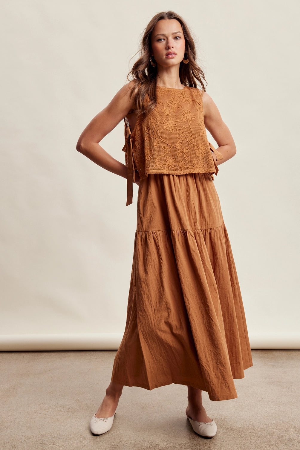 A women's brown sleeveless tiered maxi dress featuring a tonal embroidered floral lace vest overlay with adjustable side tie details.