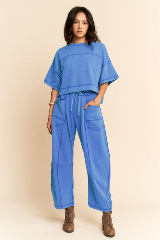 A women's two-piece lounge set in washed marina blue featuring a short-sleeve cropped top with exposed seam lines and matching high-rise wide-leg pants with a drawstring waist and utility patch pockets.