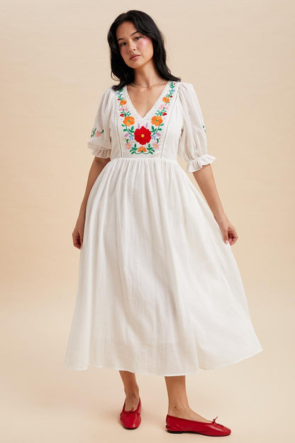 Off white maxi dress with a v-neck and embroidered bodice.  The sleeves are cuffed with a ruffle detail and hit just above the elbow with minimal embroidered detail. Waist tie in the back. 