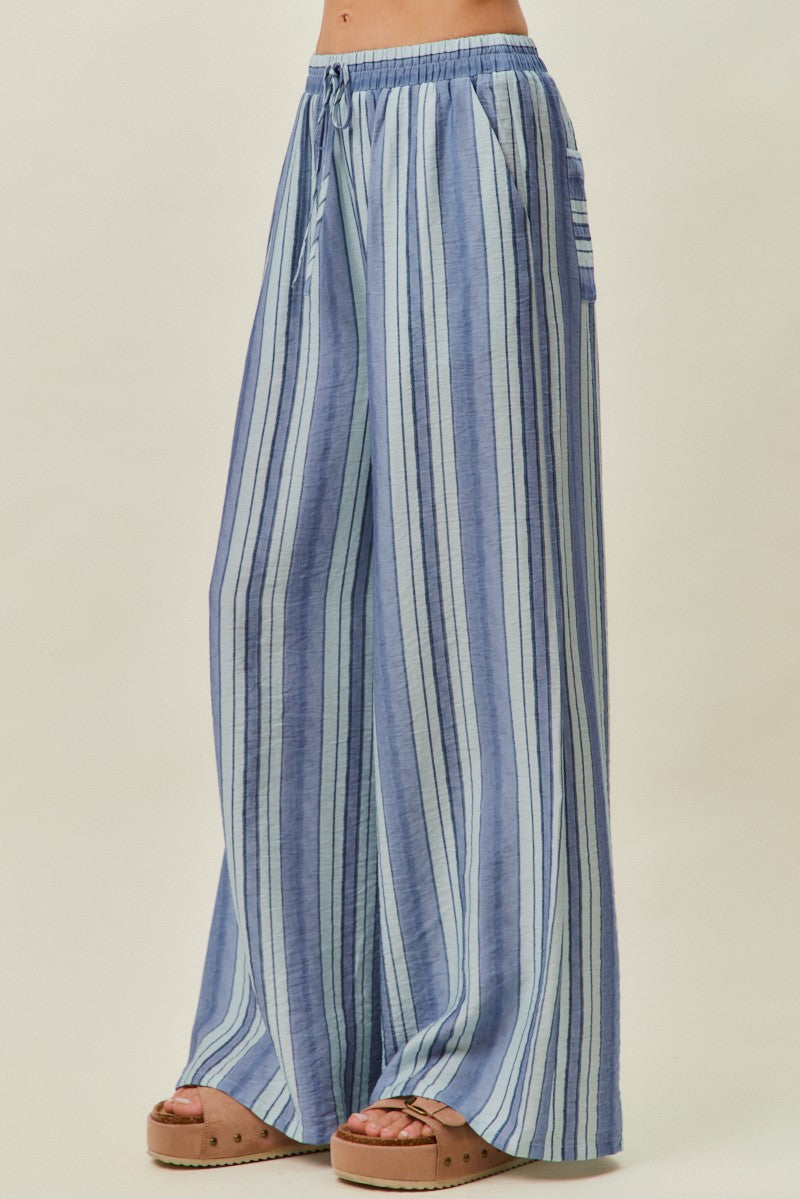A pair of women's high-waisted wide-leg pull-on pants featuring vertical stripes in shades of blue with a gathered elastic drawstring waistband and side pockets.