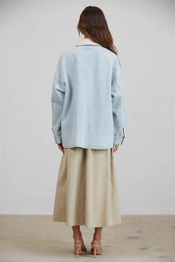 A women's relaxed oversized light wash denim utility jacket featuring a cream-colored pointed contrast collar, a button-front closure, and large front patch pockets with flaps.