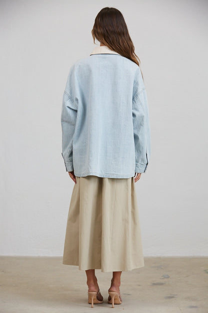 A women's relaxed oversized light wash denim utility jacket featuring a cream-colored pointed contrast collar, a button-front closure, and large front patch pockets with flaps.