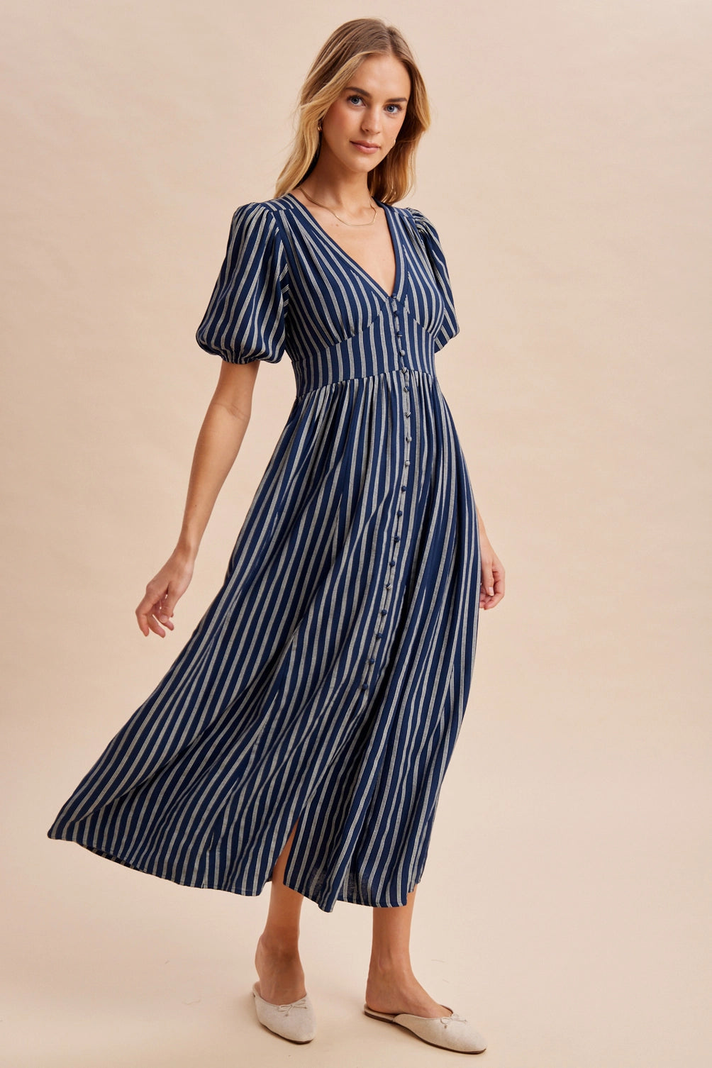 A women's navy blue and cream vertically striped short puff sleeve maxi dress featuring a V-neckline, full front button placket, and high gathered waistline.