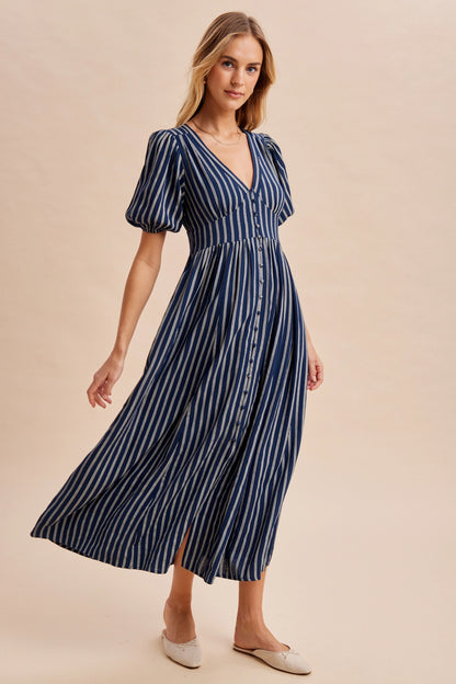 A women's navy blue and cream vertically striped short puff sleeve maxi dress featuring a V-neckline, full front button placket, and high gathered waistline.