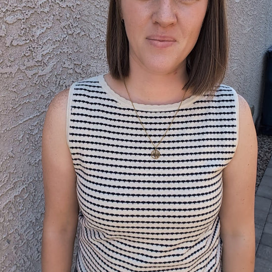 A sleeveless horizontal stripe knit sweater tank featuring a high boatneck, delicate ribbed trim at the hem and armholes, and a neutral oatmeal and navy color palette.
