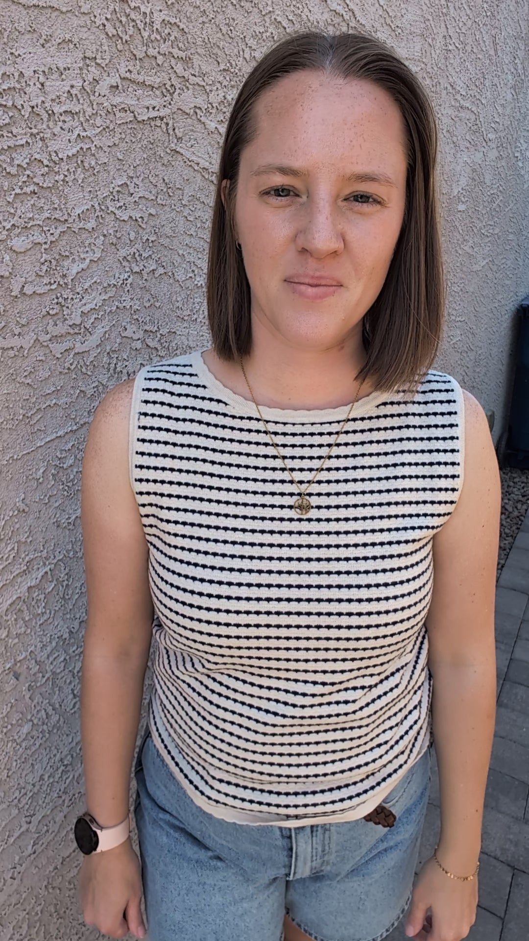 A sleeveless horizontal stripe knit sweater tank featuring a high boatneck, delicate ribbed trim at the hem and armholes, and a neutral oatmeal and navy color palette.