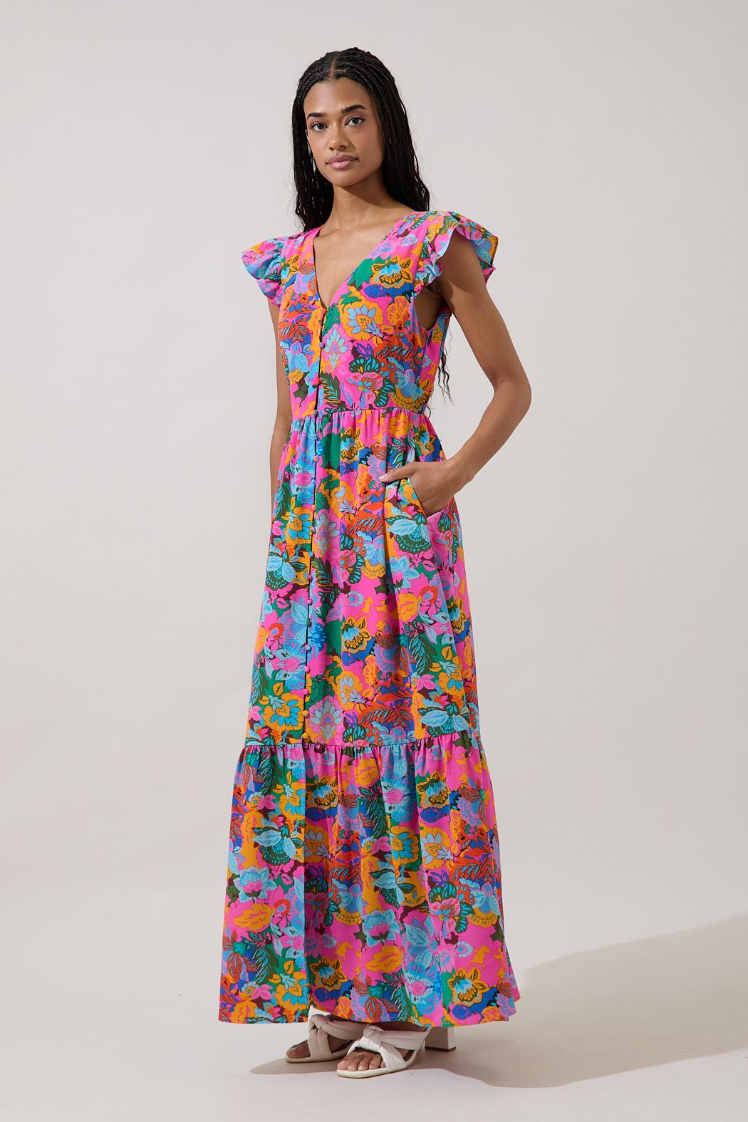 A fuchsia multi-color floral maxi dress featuring a V-neckline, functional button-down front, tiered skirt, flutter sleeves, and hidden side pockets.