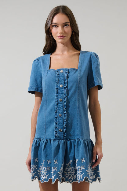 A women's medium wash blue denim short-sleeve mini dress featuring a square neckline, ruffled button placket, and cream floral embroidered scalloped hemline.